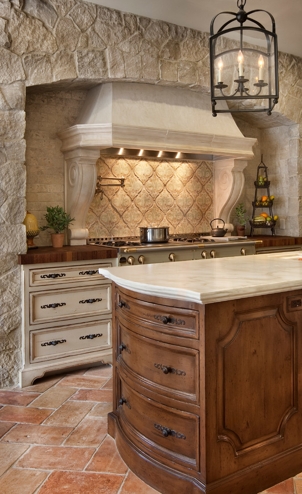 Inspiration for a large mediterranean u-shaped terra-cotta tile and red floor eat-in kitchen remodel in San Diego with a farmhouse sink, recessed-panel cabinets, distressed cabinets, marble countertops, white backsplash, stone slab backsplash, paneled appliances and an island