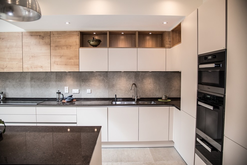 This is an example of a large contemporary l-shaped kitchen/diner in London with an integrated sink, flat-panel cabinets, medium wood cabinets, granite worktops, grey splashback, cement tile splashback, black appliances, cement flooring, an island and grey floors.