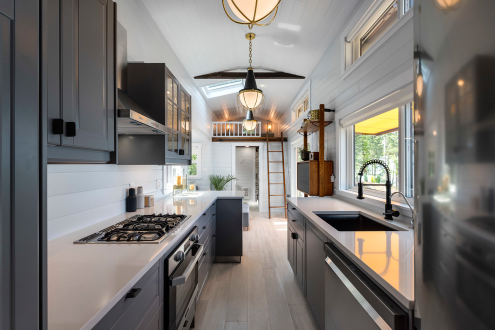 Photo of a traditional galley open plan kitchen in Vancouver with a submerged sink, raised-panel cabinets, grey cabinets, white splashback, stainless steel appliances, light hardwood flooring, beige floors and white worktops.