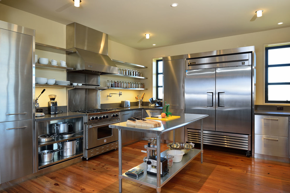 Inspiration for a large industrial u-shaped medium tone wood floor enclosed kitchen remodel in Boise with an undermount sink, flat-panel cabinets, stainless steel cabinets, stainless steel countertops, metallic backsplash, metal backsplash and stainless steel appliances