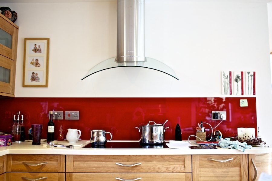ロンドンにある中くらいなカントリー風のおしゃれなキッチン (アンダーカウンターシンク、シェーカースタイル扉のキャビネット、ベージュのキャビネット、人工大理石カウンター、赤いキッチンパネル、ガラス板のキッチンパネル、シルバーの調理設備、無垢フローリング、ベージュの床、白いキッチンカウンター) の写真