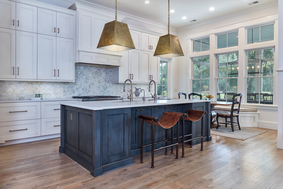Inspiration for a large transitional l-shaped medium tone wood floor and brown floor eat-in kitchen remodel in Charleston with an undermount sink, gray backsplash, ceramic backsplash, stainless steel appliances, an island, white cabinets and white countertops