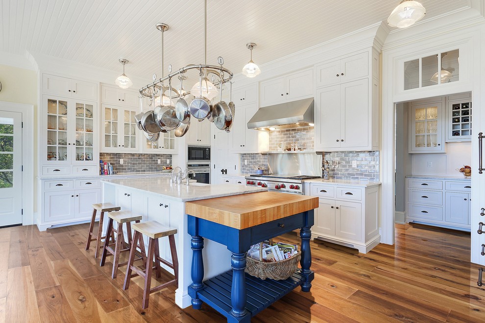 Inspiration for a timeless l-shaped medium tone wood floor and brown floor kitchen remodel in San Francisco with a farmhouse sink, shaker cabinets, white cabinets, gray backsplash, stainless steel appliances, an island and white countertops