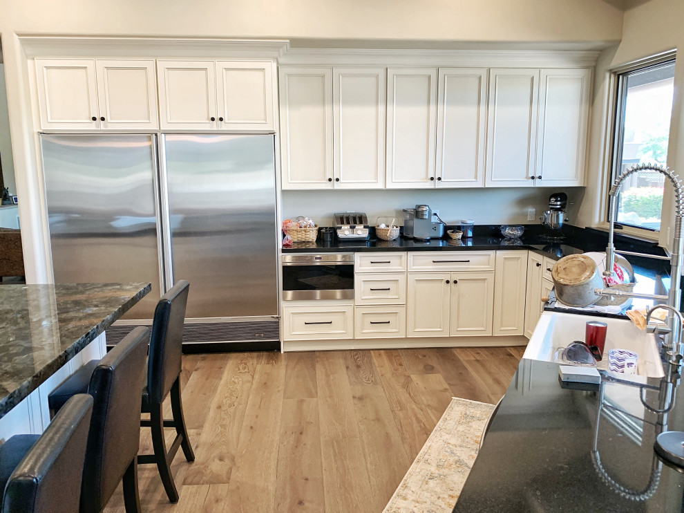 Example of a huge transitional u-shaped light wood floor and beige floor eat-in kitchen design in Phoenix with a farmhouse sink, flat-panel cabinets, white cabinets, quartz countertops, white backsplash, glass tile backsplash, stainless steel appliances, an island and black countertops