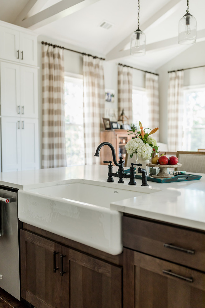 Photo of a country kitchen in Atlanta with a belfast sink, shaker cabinets, white cabinets, engineered stone countertops, white splashback, ceramic splashback, stainless steel appliances, dark hardwood flooring, an island, brown floors and white worktops.