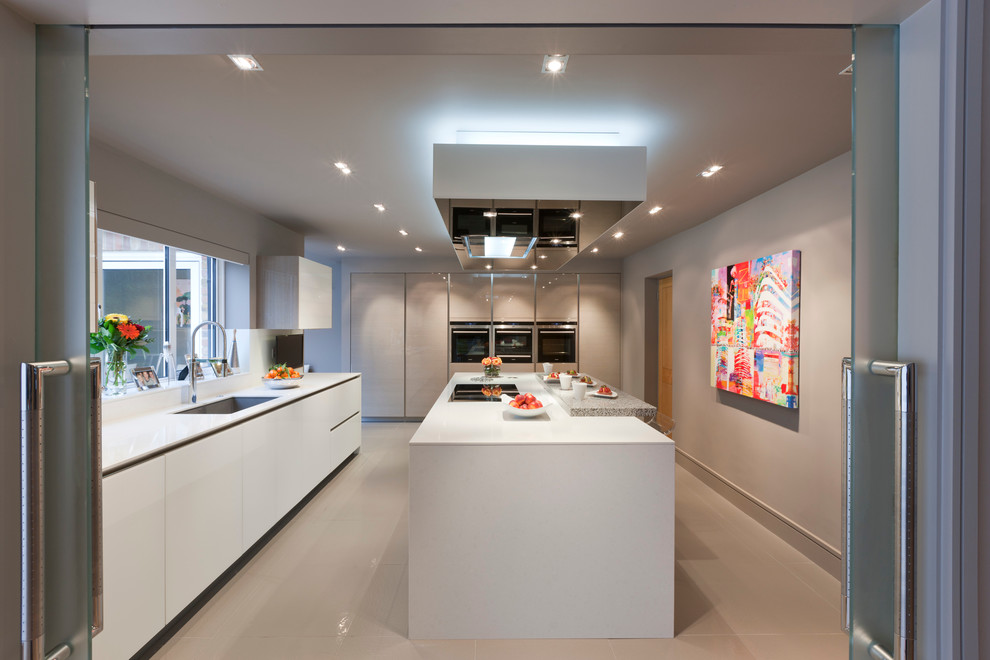 This is an example of a large contemporary enclosed kitchen in London with a submerged sink, flat-panel cabinets, white cabinets, integrated appliances and an island.