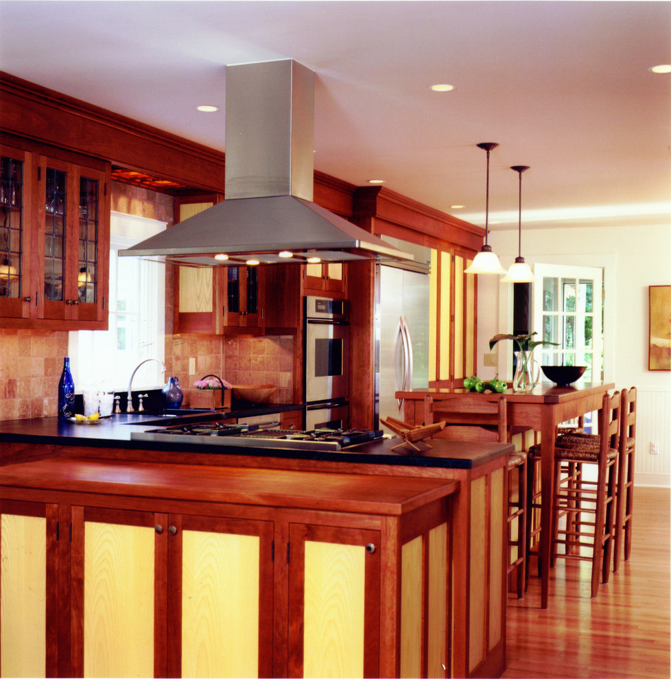 Example of a mid-sized classic l-shaped light wood floor kitchen pantry design in Boston with glass-front cabinets, medium tone wood cabinets, beige backsplash, stainless steel appliances and a peninsula