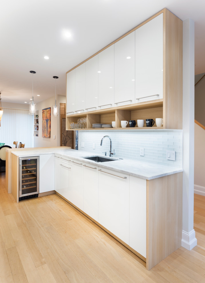 Ejemplo de cocina comedor actual de tamaño medio con fregadero encastrado, armarios con paneles lisos, puertas de armario de madera oscura, encimera de cuarzo compacto, salpicadero blanco, salpicadero de azulejos de vidrio, suelo de madera clara y península