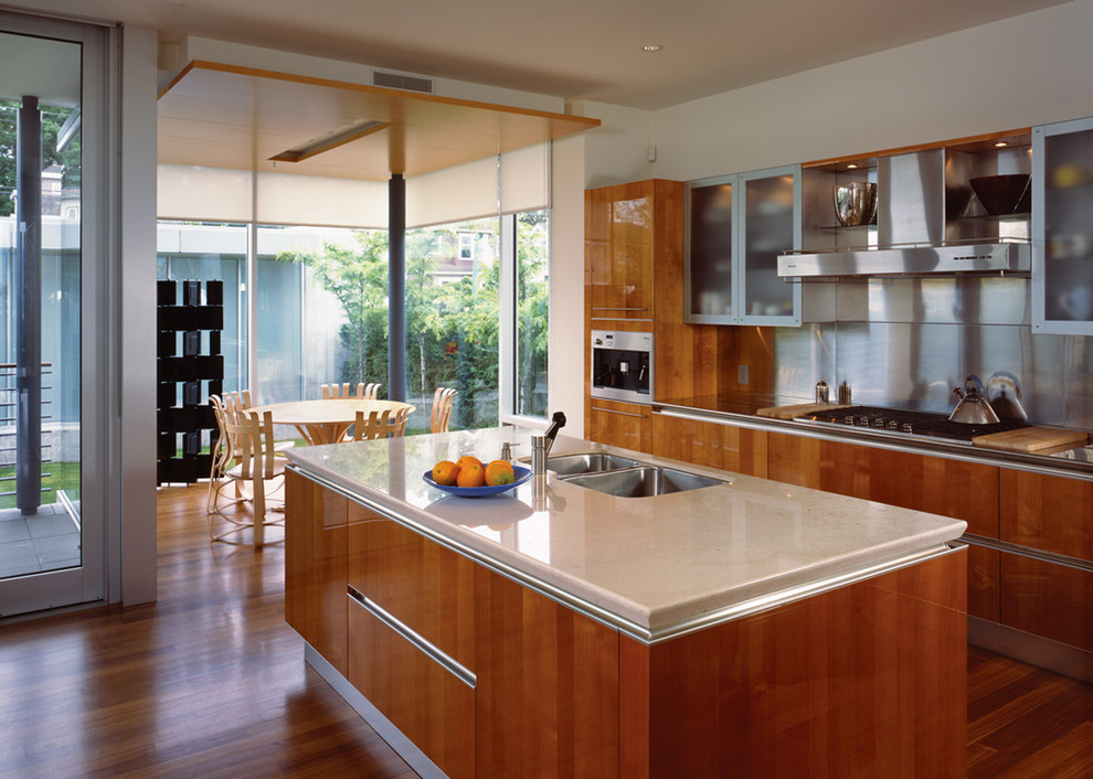 Modern inredning av ett kök, med rostfria vitvaror, en dubbel diskho, bruna skåp, stänkskydd med metallisk yta och stänkskydd i metallkakel