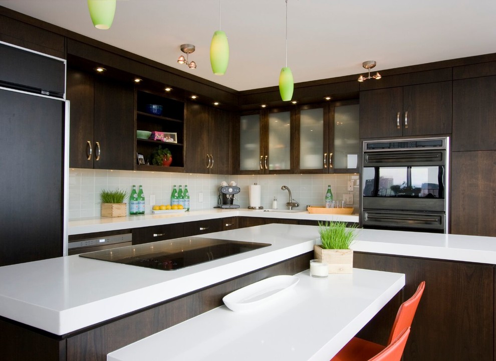 This is an example of a medium sized contemporary l-shaped kitchen in Milwaukee with a submerged sink, flat-panel cabinets, dark wood cabinets, composite countertops, white splashback, black appliances, an island, glass tiled splashback, bamboo flooring and brown floors.