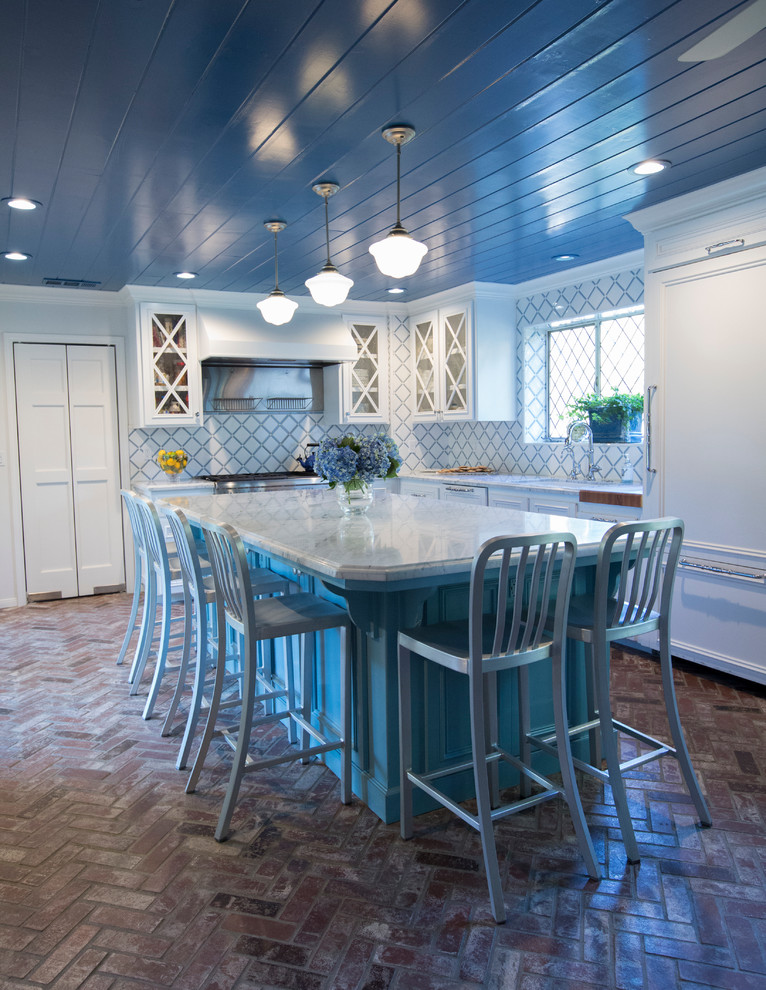Inredning av ett klassiskt kök, med vita skåp, blått stänkskydd, stänkskydd i keramik, tegelgolv och en köksö