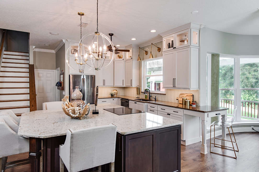 Idée de décoration pour une grande cuisine américaine bicolore design en L avec un évier encastré, un placard à porte shaker, des portes de placard blanches, une crédence beige, îlot, un plan de travail en quartz, un électroménager en acier inoxydable, un sol en bois brun, un plan de travail multicolore, une crédence en feuille de verre et un sol marron.