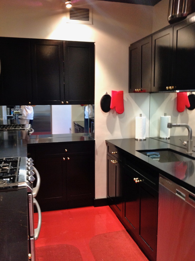Aménagement d'une petite cuisine parallèle fermée avec un évier encastré, des portes de placard noires, un plan de travail en surface solide, une crédence miroir, un électroménager en acier inoxydable, un sol en linoléum, aucun îlot et un sol rouge.