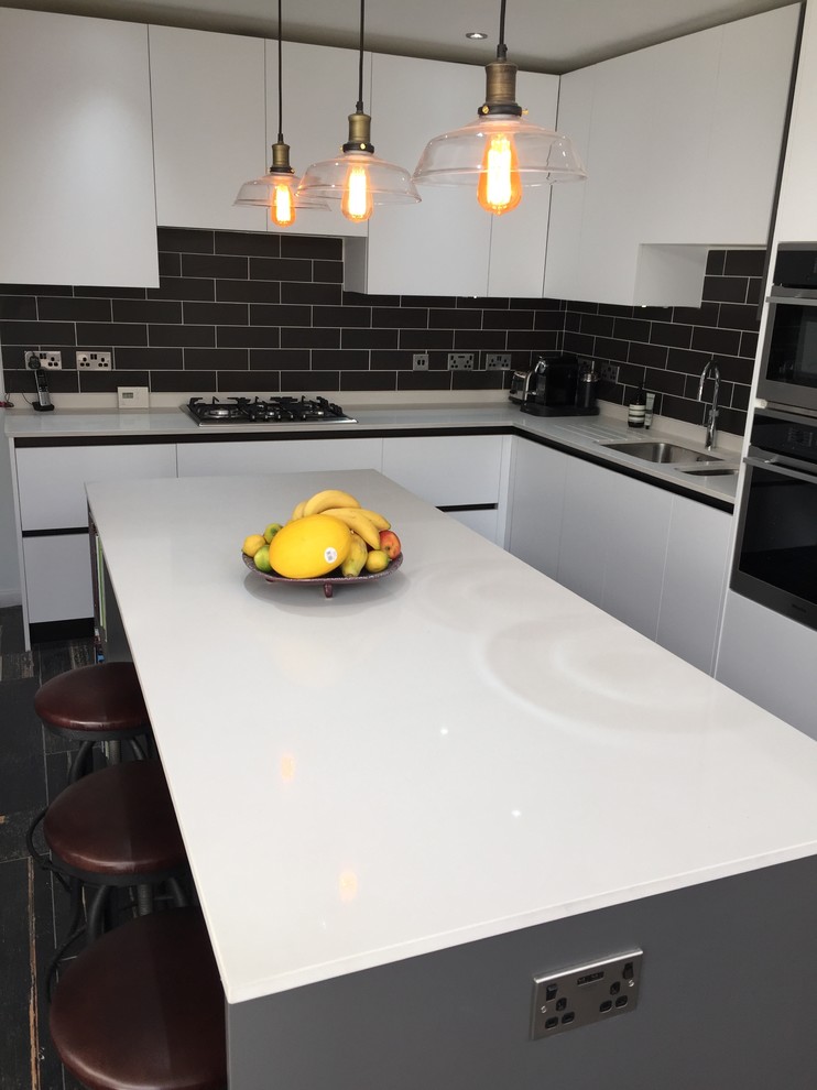 This is an example of a medium sized urban l-shaped kitchen/diner in Hertfordshire with a double-bowl sink, flat-panel cabinets, white cabinets, quartz worktops, black splashback, ceramic splashback, stainless steel appliances, porcelain flooring and an island.