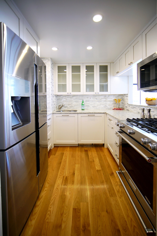Eat-in kitchen - transitional u-shaped plywood floor and brown floor eat-in kitchen idea in New York with a drop-in sink, flat-panel cabinets, white cabinets, marble countertops, gray backsplash, mosaic tile backsplash, white appliances, no island and white countertops