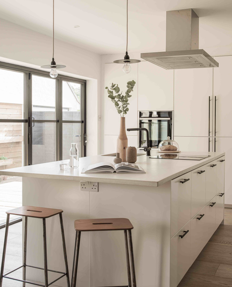 Design ideas for a medium sized scandi u-shaped open plan kitchen in Essex with flat-panel cabinets, white cabinets, concrete worktops, black appliances, an island and grey worktops.