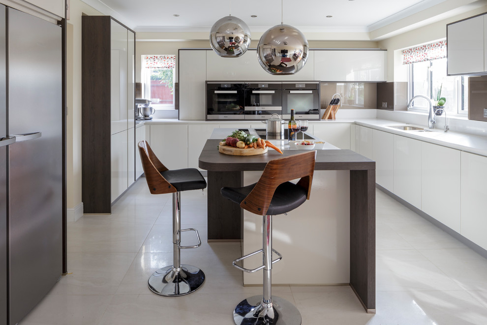 Moderne Küche mit weißen Schränken, Quarzit-Arbeitsplatte, Küchenrückwand in Braun, Glasrückwand, schwarzen Elektrogeräten und Kücheninsel in Berkshire