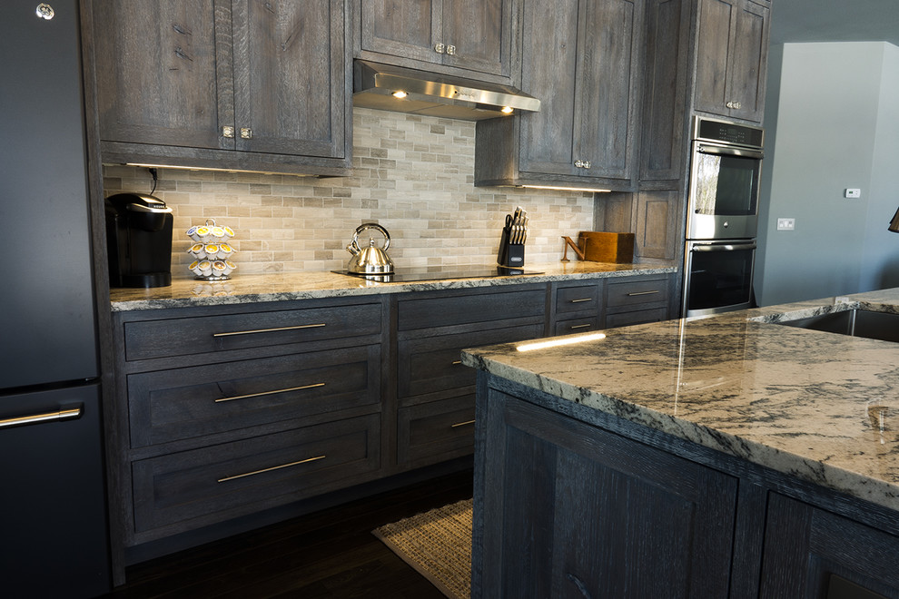 Example of a mid-sized urban single-wall dark wood floor and black floor open concept kitchen design in Other with an undermount sink, recessed-panel cabinets, distressed cabinets, granite countertops, beige backsplash, ceramic backsplash, stainless steel appliances and an island