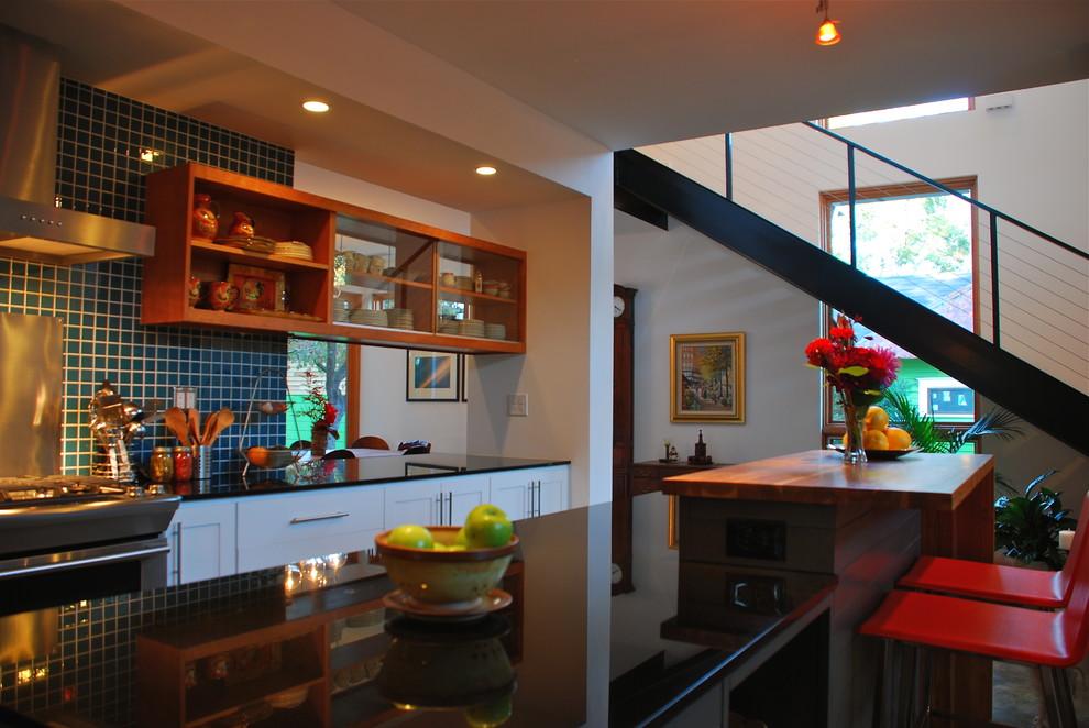 Inredning av ett modernt litet kök, med blått stänkskydd, rostfria vitvaror, betonggolv och en köksö