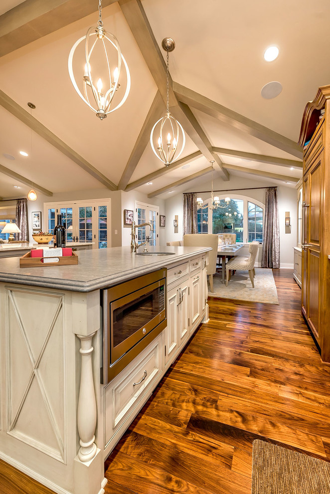 Example of a mid-sized trendy l-shaped medium tone wood floor open concept kitchen design in San Francisco with a farmhouse sink, recessed-panel cabinets, gray cabinets, quartzite countertops, gray backsplash, stone tile backsplash, stainless steel appliances and two islands