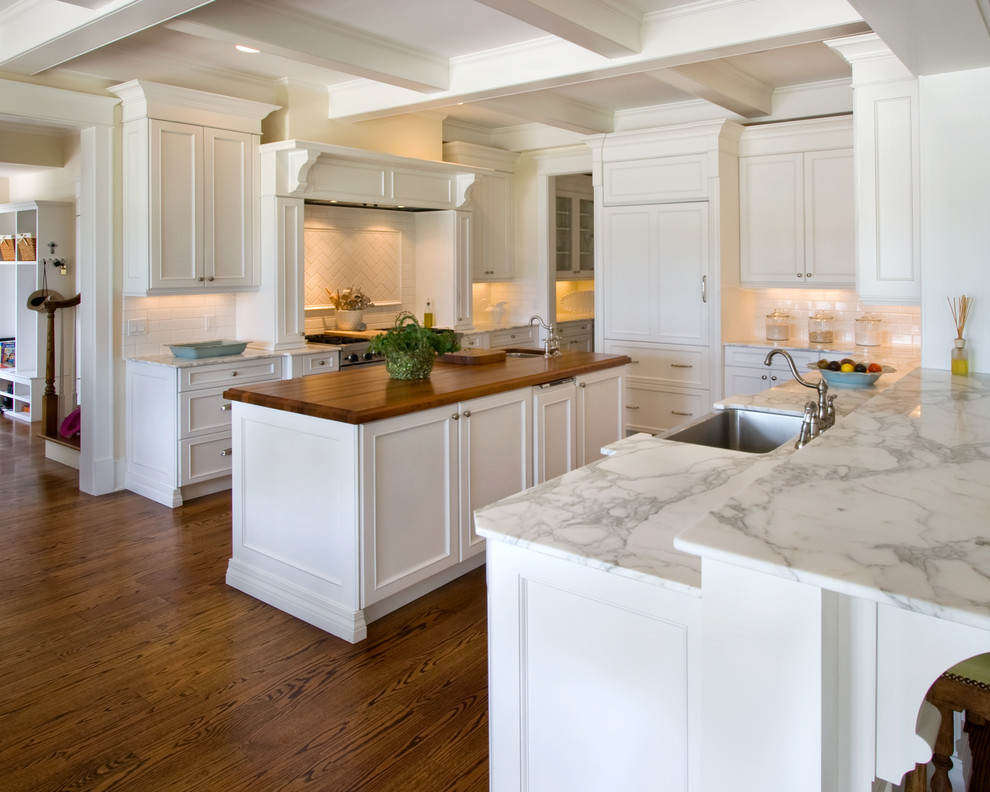Photo of an expansive victorian l-shaped kitchen/diner in Orlando with a belfast sink, shaker cabinets, white cabinets, marble worktops, white splashback, metro tiled splashback, stainless steel appliances, dark hardwood flooring, an island and brown floors.