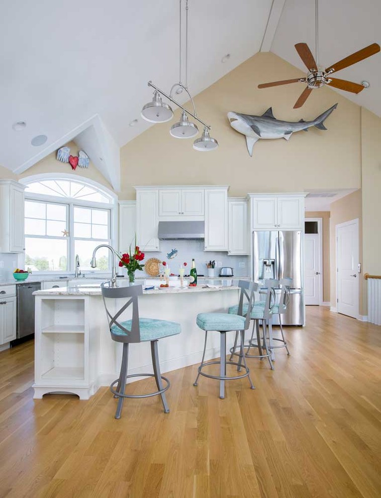 Inspiration for a large coastal l-shaped medium tone wood floor kitchen remodel in Other with an undermount sink, raised-panel cabinets, white cabinets, white backsplash, subway tile backsplash, stainless steel appliances and an island