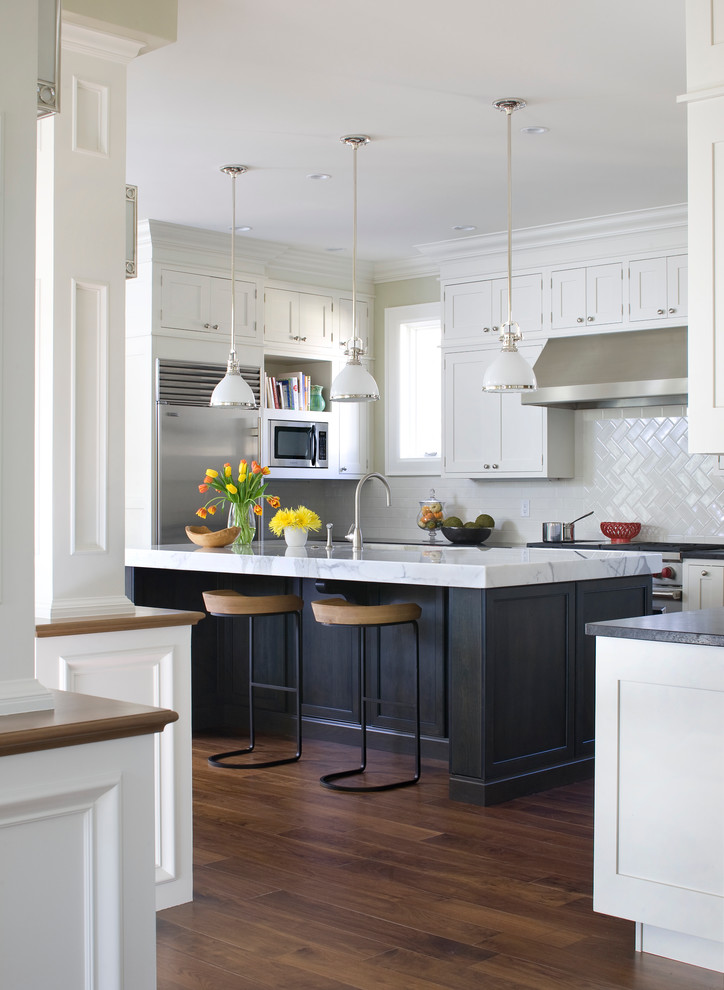 Cette photo montre une cuisine chic en U avec un placard à porte shaker, des portes de placard blanches, une crédence blanche et un électroménager en acier inoxydable.