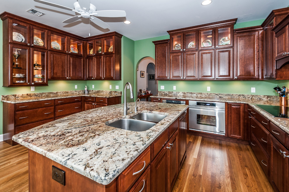Eat-in kitchen - traditional u-shaped eat-in kitchen idea in Tampa with a double-bowl sink, raised-panel cabinets, dark wood cabinets, granite countertops, multicolored backsplash and stainless steel appliances