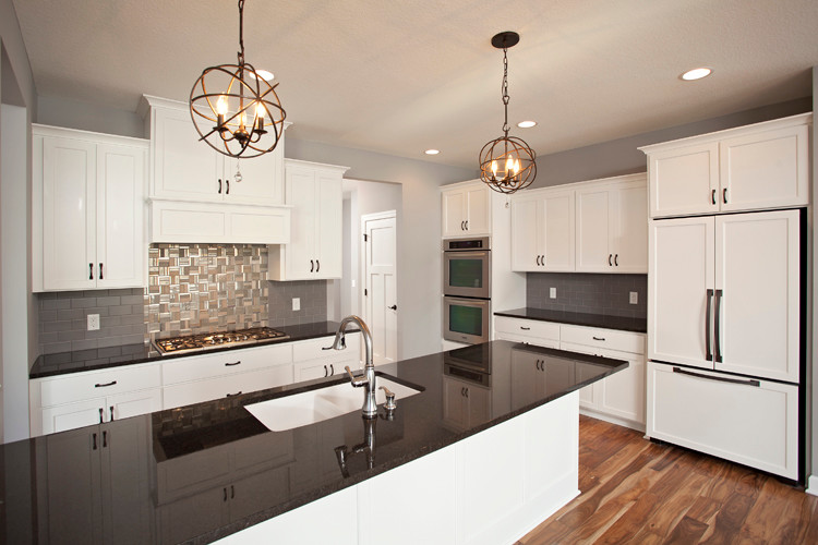 Inspiration for a large transitional l-shaped medium tone wood floor and brown floor open concept kitchen remodel in Minneapolis with an undermount sink, flat-panel cabinets, white cabinets, granite countertops, gray backsplash, paneled appliances, ceramic backsplash, a peninsula and black countertops