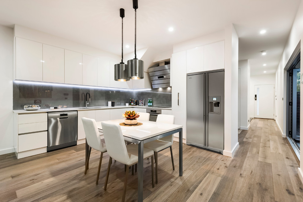 Moderne Wohnküche ohne Insel in L-Form mit Unterbauwaschbecken, flächenbündigen Schrankfronten, weißen Schränken und hellem Holzboden in Melbourne