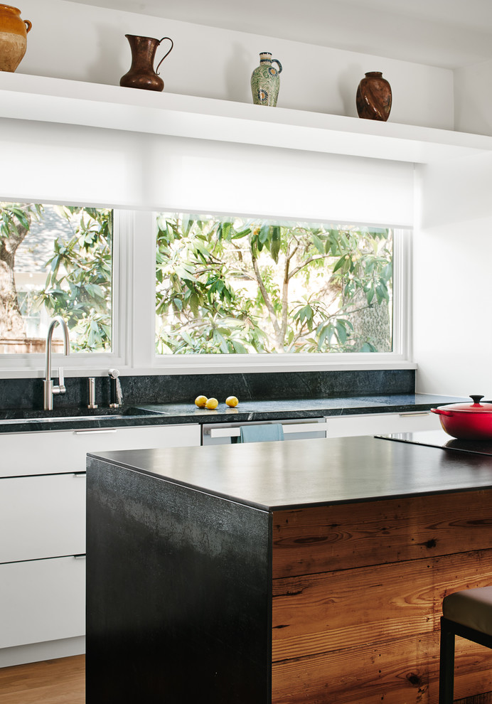 Rustik inredning av ett svart svart kök, med en undermonterad diskho, släta luckor, vita skåp, fönster som stänkskydd och en köksö