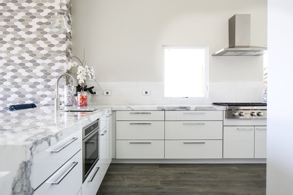 Medium sized contemporary l-shaped open plan kitchen in Orange County with a built-in sink, flat-panel cabinets, white cabinets, marble worktops, white splashback, stone tiled splashback, stainless steel appliances, porcelain flooring and a breakfast bar.