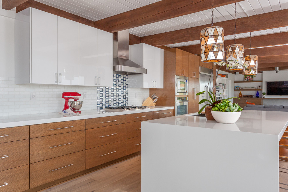 Inspiration for a medium sized retro single-wall open plan kitchen in Orange County with a single-bowl sink, flat-panel cabinets, medium wood cabinets, engineered stone countertops, white splashback, glass tiled splashback, stainless steel appliances, medium hardwood flooring and an island.