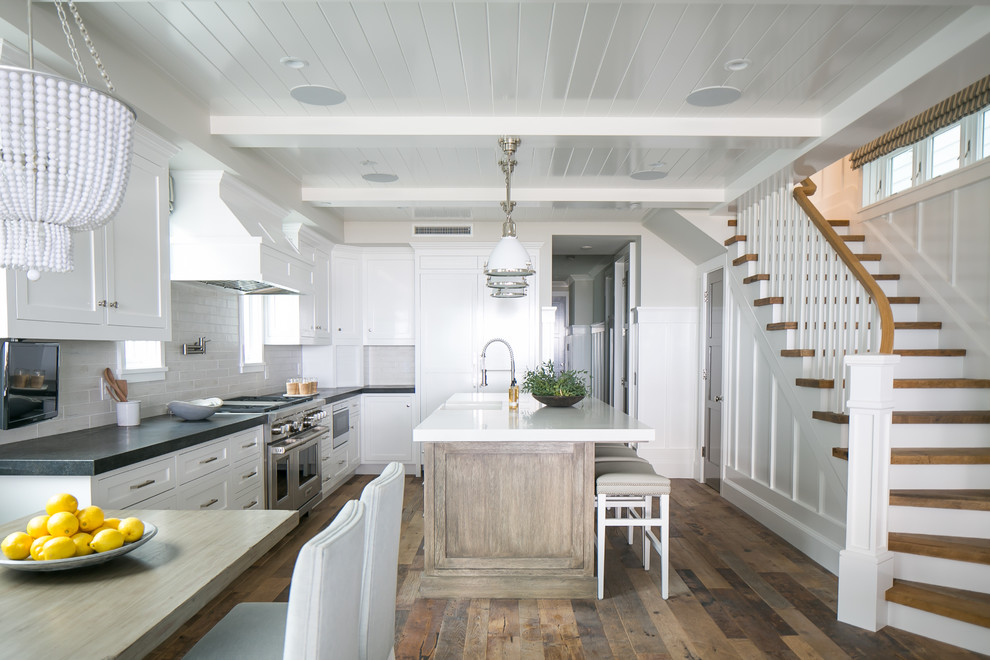 Open concept kitchen - mid-sized coastal l-shaped medium tone wood floor and brown floor open concept kitchen idea in Orange County with a farmhouse sink, shaker cabinets, white cabinets, concrete countertops, white backsplash, ceramic backsplash, stainless steel appliances and an island