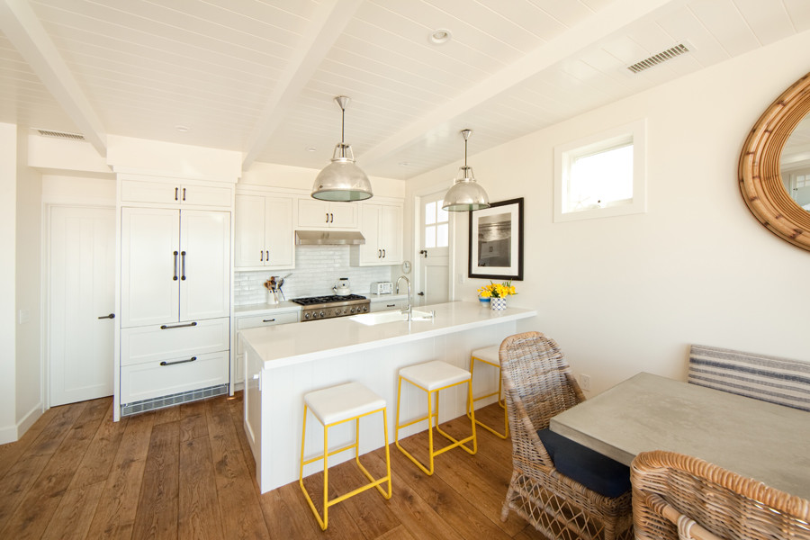 Bild på ett mellanstort maritimt kök, med en rustik diskho, skåp i shakerstil, vita skåp, bänkskiva i kvarts, vitt stänkskydd, stänkskydd i stickkakel, vita vitvaror, ljust trägolv och en halv köksö