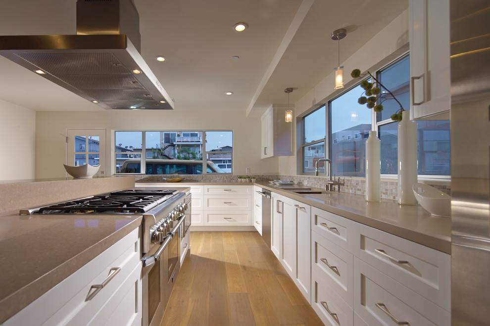 Medium sized contemporary galley kitchen/diner in Orange County with an integrated sink, recessed-panel cabinets, white cabinets, composite countertops, ceramic splashback, stainless steel appliances, light hardwood flooring, an island and grey splashback.