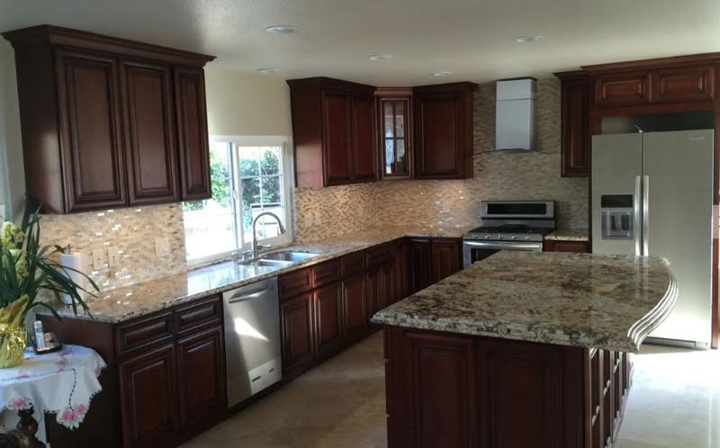 Example of a large classic l-shaped ceramic tile and beige floor enclosed kitchen design in Orange County with a double-bowl sink, raised-panel cabinets, dark wood cabinets, granite countertops, beige backsplash, glass tile backsplash, stainless steel appliances and an island