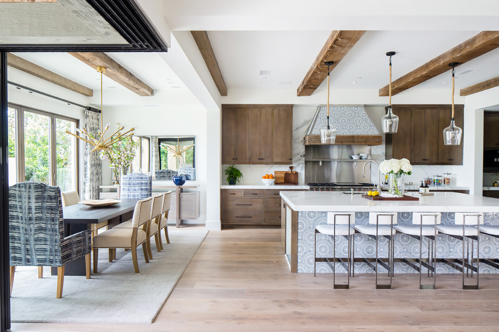 Inspiration for a large mediterranean l-shaped open plan kitchen in Orange County with a submerged sink, flat-panel cabinets, medium wood cabinets, white splashback, stainless steel appliances, medium hardwood flooring, an island, brown floors and white worktops.