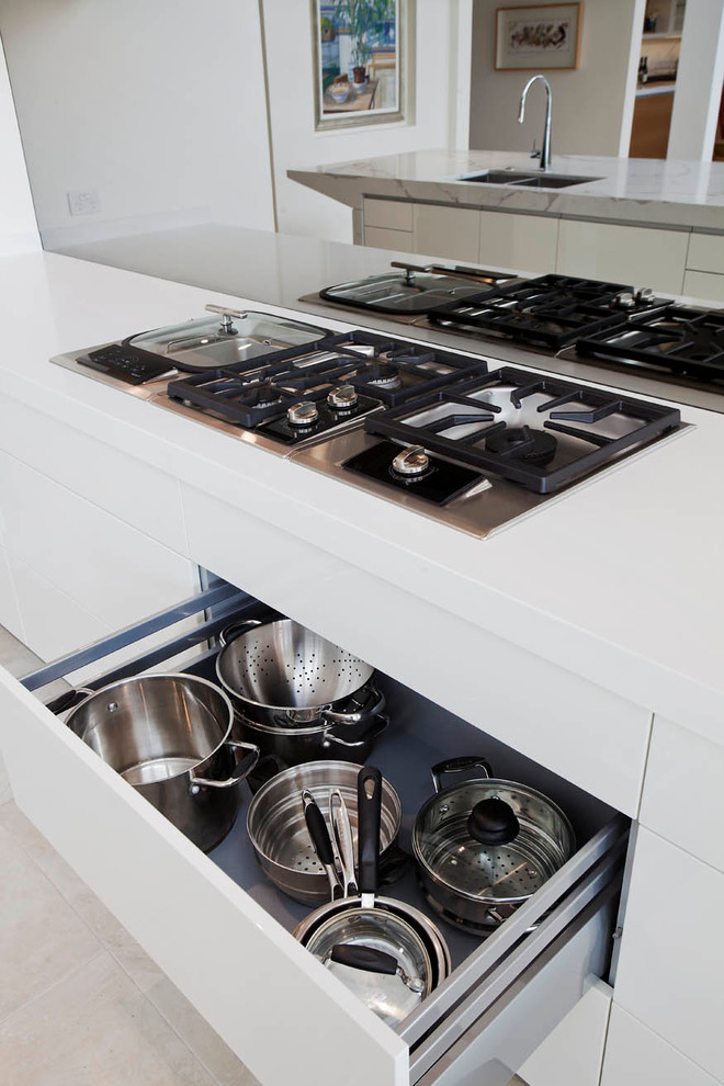 Large modern l-shaped open plan kitchen in Sydney with a submerged sink, flat-panel cabinets, white cabinets, engineered stone countertops, grey splashback, mirror splashback, black appliances, limestone flooring and an island.