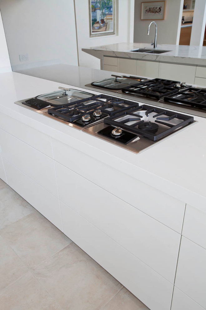 This is an example of a large modern l-shaped open plan kitchen in Sydney with a submerged sink, flat-panel cabinets, white cabinets, engineered stone countertops, grey splashback, mirror splashback, black appliances, limestone flooring and an island.