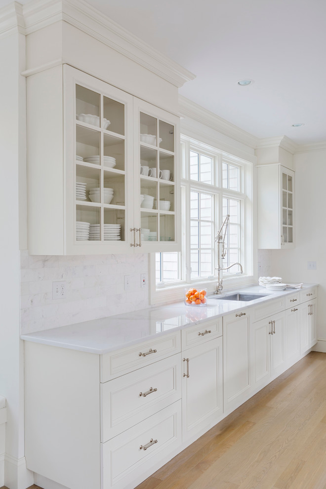 Example of a large transitional l-shaped light wood floor open concept kitchen design in Providence with shaker cabinets, white cabinets, white backsplash, paneled appliances, an island, an undermount sink, marble countertops and stone tile backsplash