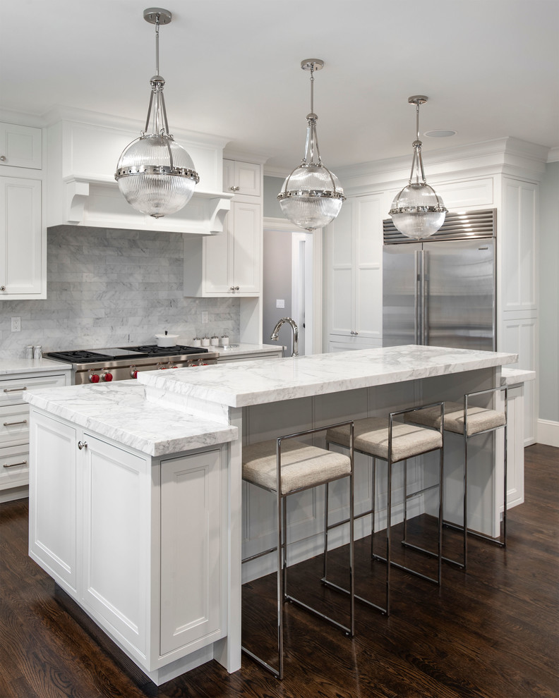 Photo of an expansive traditional l-shaped kitchen/diner in Boston with a submerged sink, beaded cabinets, white cabinets, marble worktops, grey splashback, marble splashback, stainless steel appliances, dark hardwood flooring, an island, brown floors and white worktops.