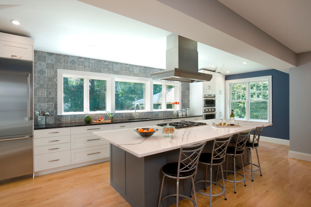 Mid-sized minimalist single-wall light wood floor and brown floor open concept kitchen photo in Boston with an undermount sink, shaker cabinets, white cabinets, granite countertops, gray backsplash, porcelain backsplash, stainless steel appliances, an island and multicolored countertops