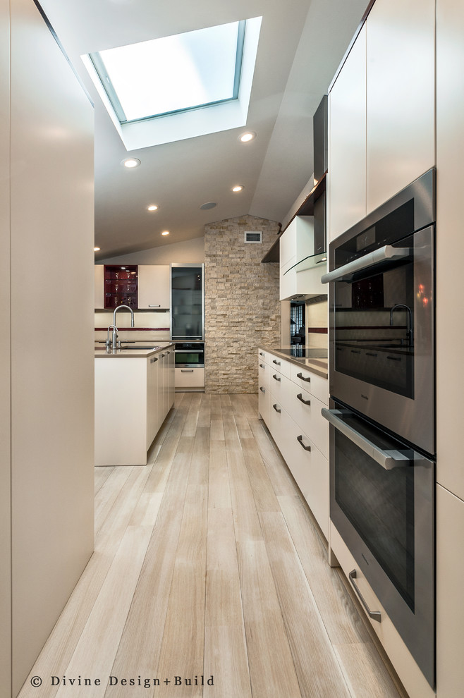 Expansive contemporary u-shaped kitchen/diner in Boston with a submerged sink, flat-panel cabinets, white cabinets, engineered stone countertops, white splashback, glass sheet splashback, stainless steel appliances, an island and light hardwood flooring.