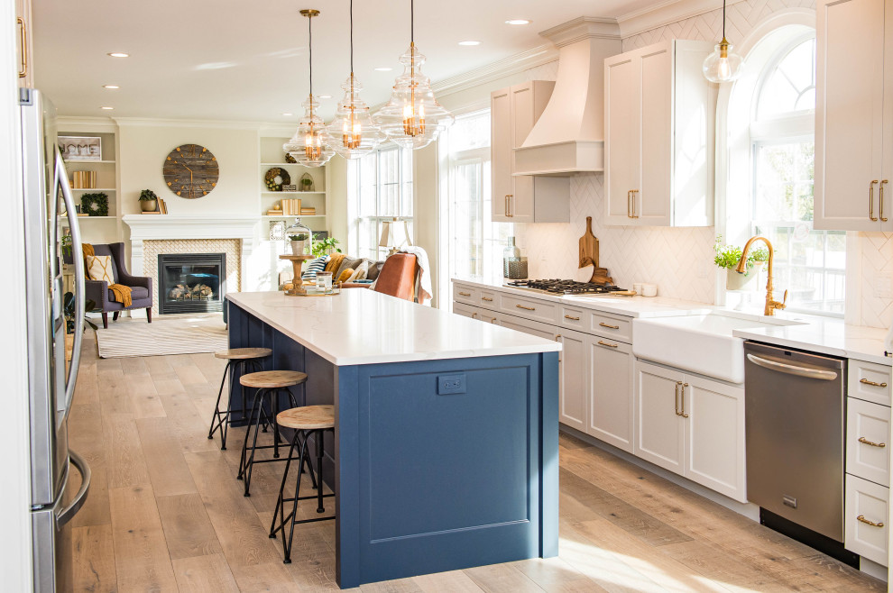 Kitchen - transitional galley medium tone wood floor and brown floor kitchen idea in Philadelphia with a farmhouse sink, shaker cabinets, white cabinets, white backsplash, stainless steel appliances, an island and white countertops