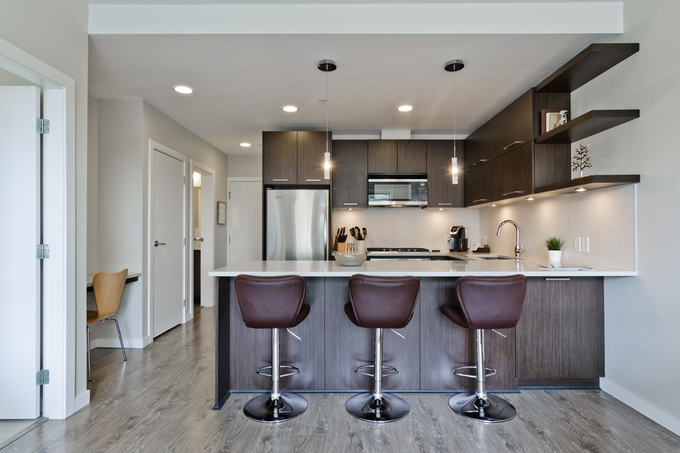 Trendy u-shaped medium tone wood floor open concept kitchen photo in Calgary with an undermount sink, flat-panel cabinets, dark wood cabinets, white backsplash, stainless steel appliances and a peninsula