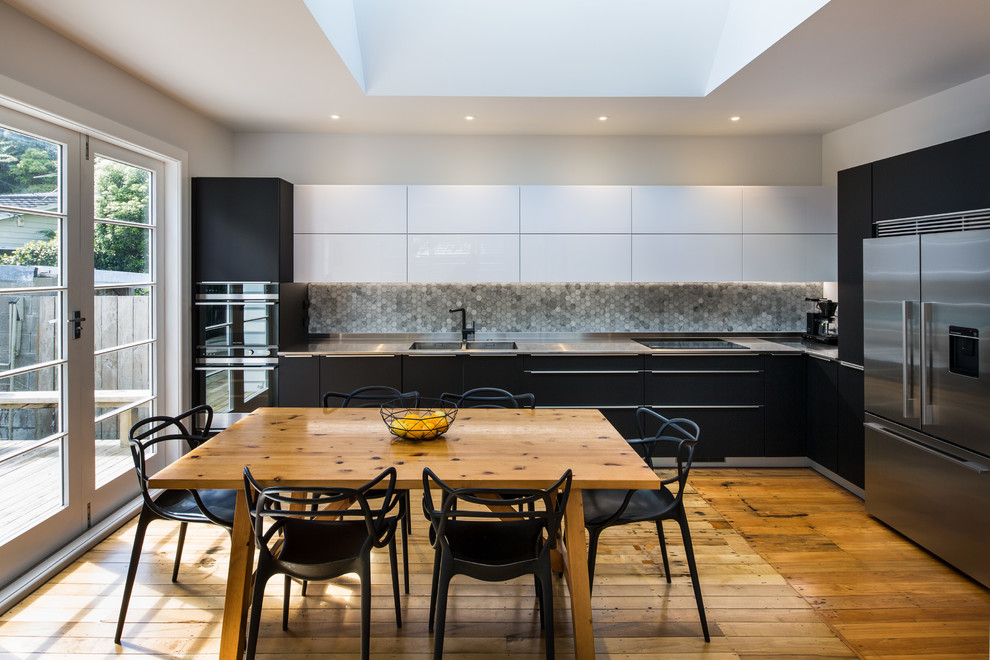Modern inredning av ett kök, med en integrerad diskho, släta luckor, svarta skåp, grått stänkskydd, stänkskydd i mosaik, rostfria vitvaror och mellanmörkt trägolv