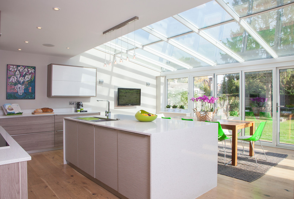 Offene Moderne Küche in L-Form mit flächenbündigen Schrankfronten, hellen Holzschränken, Küchenrückwand in Weiß, hellem Holzboden und Kücheninsel in Surrey