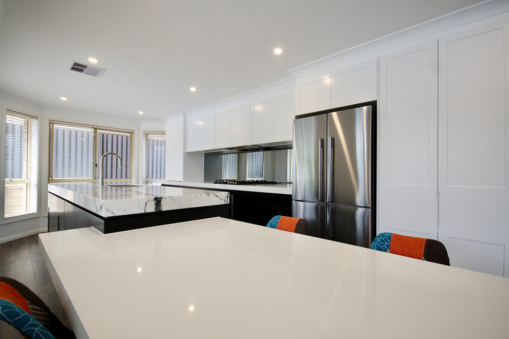 Modern inredning av ett stort vit linjärt vitt kök med öppen planlösning, med en undermonterad diskho, skåp i shakerstil, svarta skåp, marmorbänkskiva, grått stänkskydd, spegel som stänkskydd, rostfria vitvaror, mellanmörkt trägolv, en köksö och brunt golv