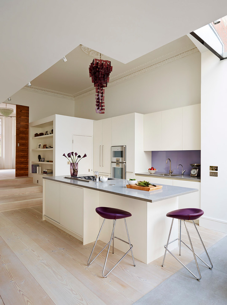 Modern inredning av ett stort brun linjärt brunt kök med öppen planlösning, med släta luckor, vita skåp, bänkskiva i kvartsit, stänkskydd i glaskakel, rostfria vitvaror, ljust trägolv, en köksö och beiget golv